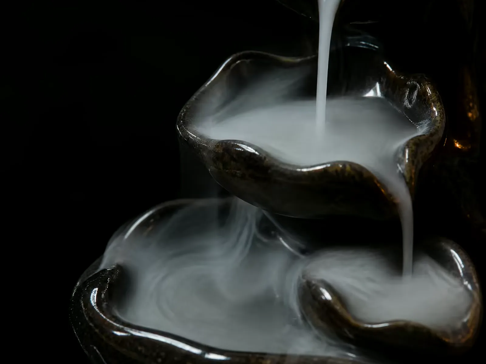 Smoke from a backflow cone running down the tiers of a dark ceramic burner