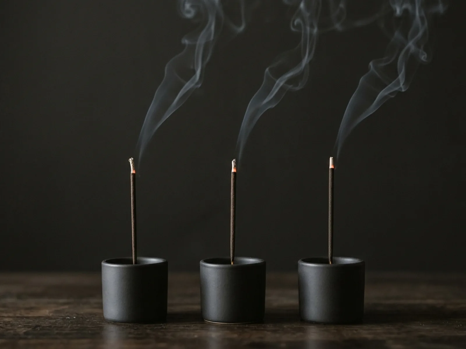 Three incense sticks burning side by side in identical holders against a plain dark background for a comparison panel