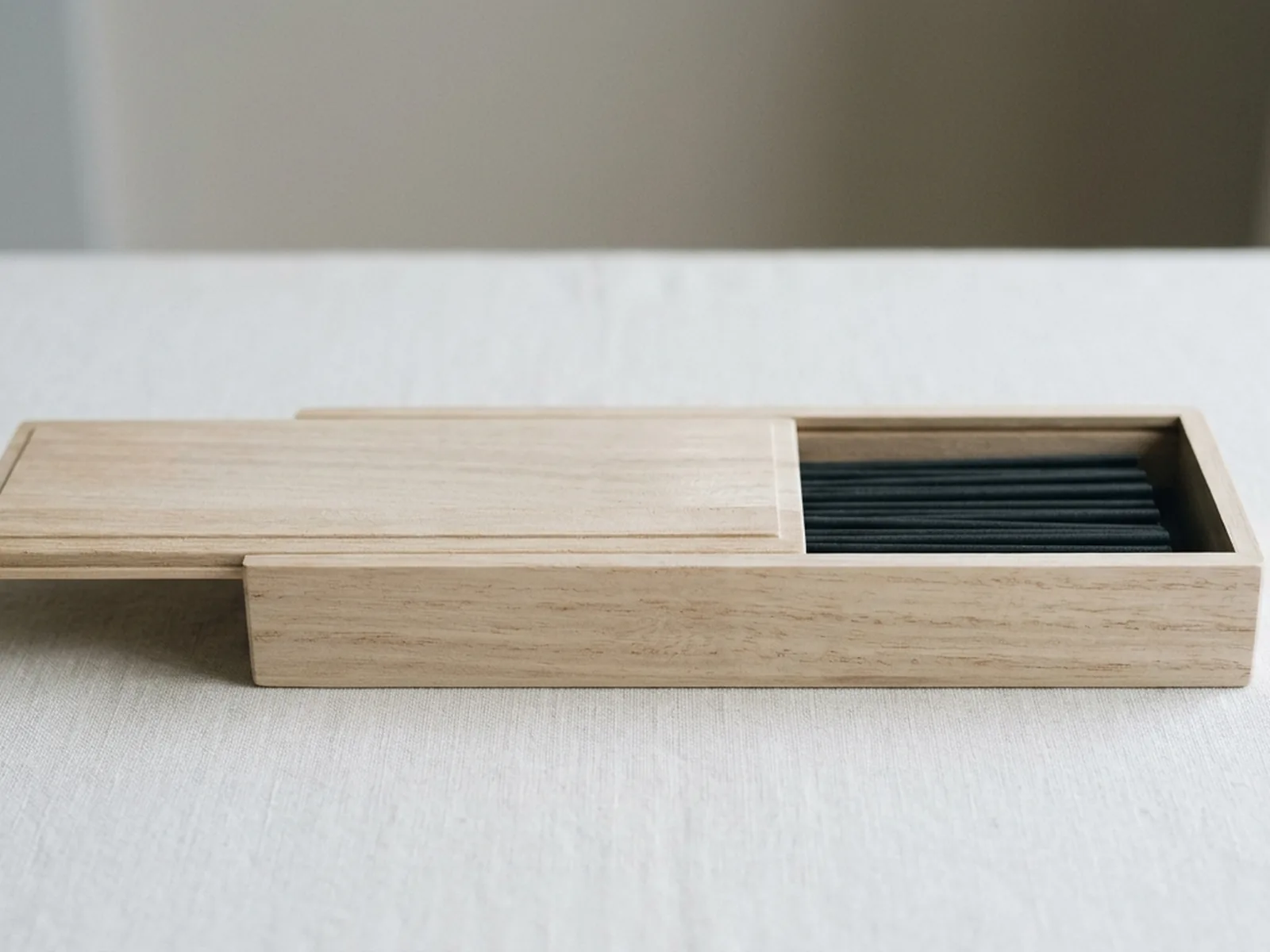 A slim pale paulownia wood box with a sliding lid, open to show short incense sticks aligned inside