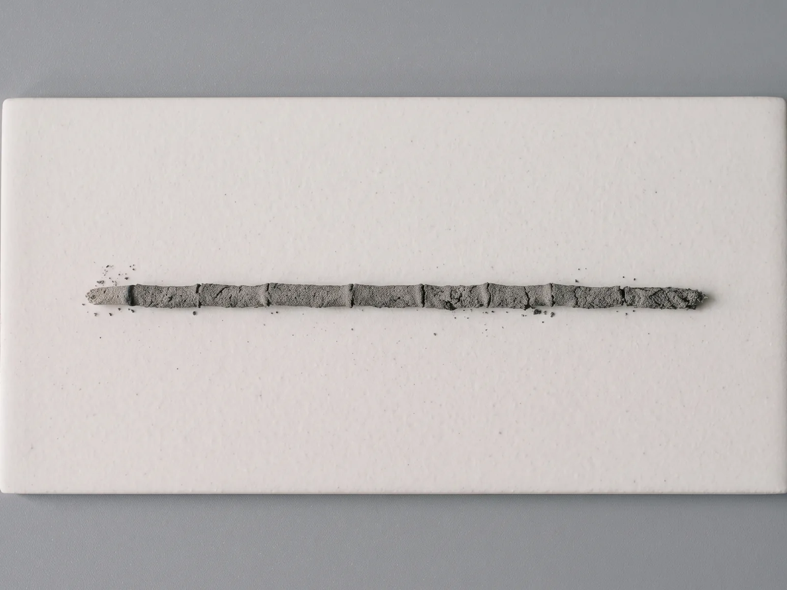 One incense stick burned to completion, its full length converted to an intact grey ash column on a white tile