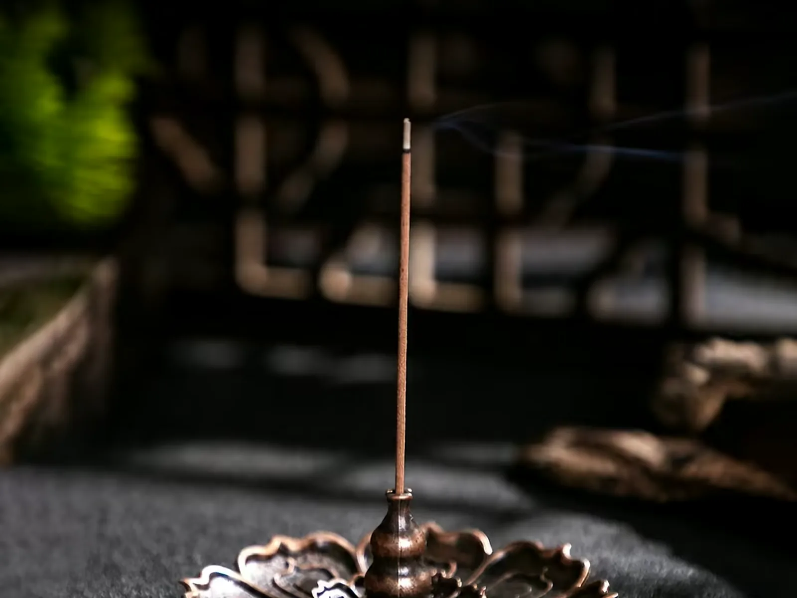 Stick burning on the brass lotus incense stand, ash falling to the disc below