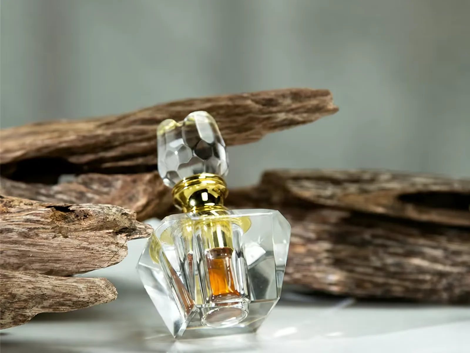 Crystal tola flask against raw agarwood, the oil colour readable through the facets