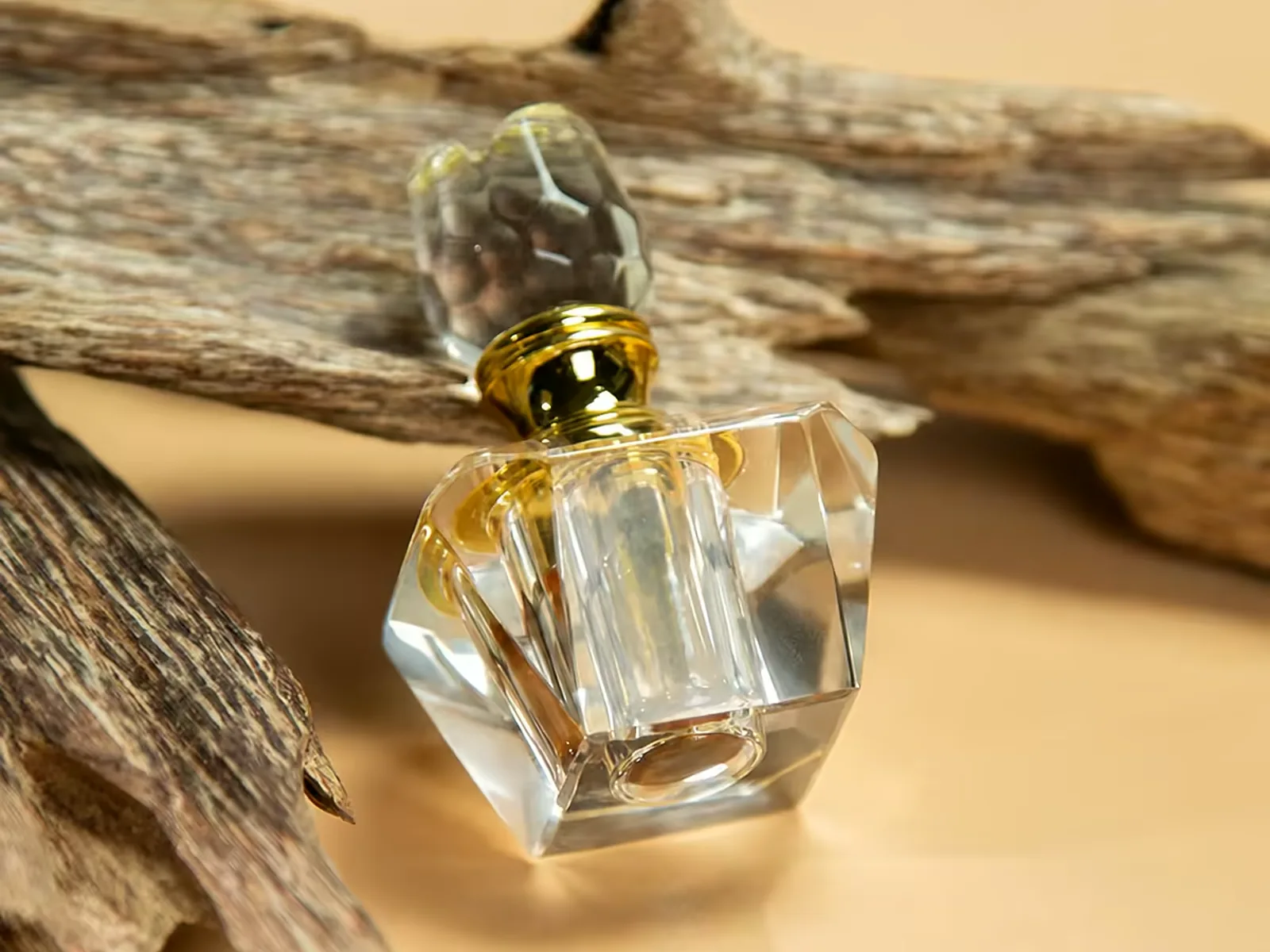 Faceted crystal tola attar flask filled with oud oil, resting against agarwood chips