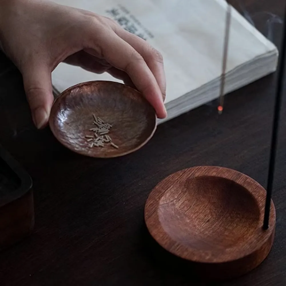 Agarwood incense material in a wooden dish beside a burning stick on its holder