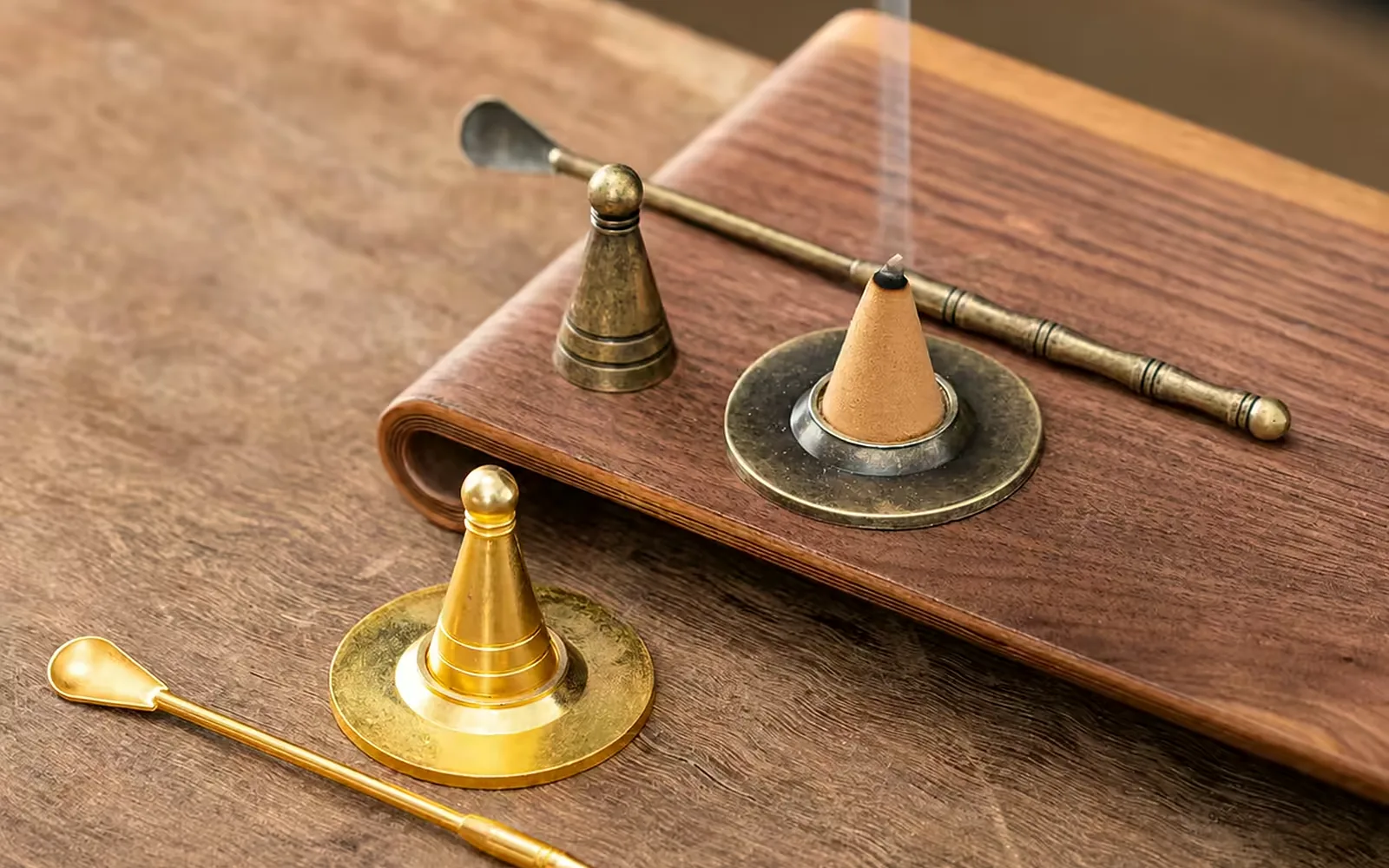 A single agarwood incense cone burning on a recessed brass dish, with brass snuffers and tools