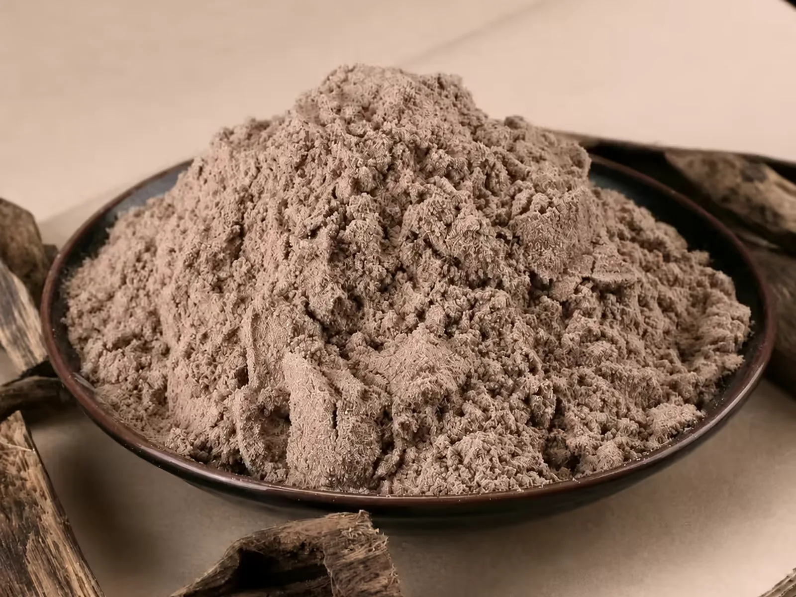 Mound of pure agarwood incense powder in a dark dish, beside resinous agarwood chips