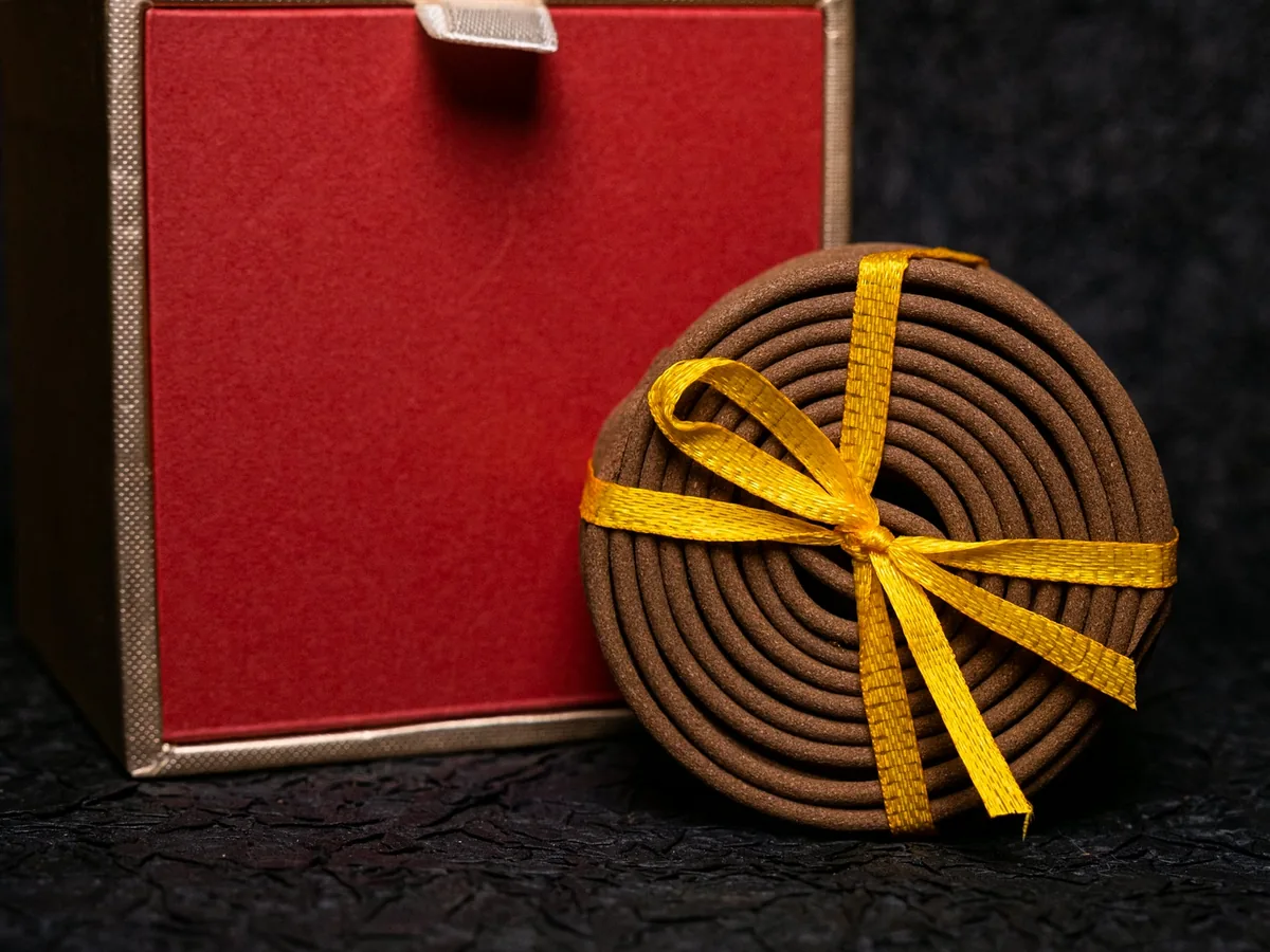 Gold-edged rim and red velvet face of the rigid gift box, a ribboned agarwood coil standing beside it