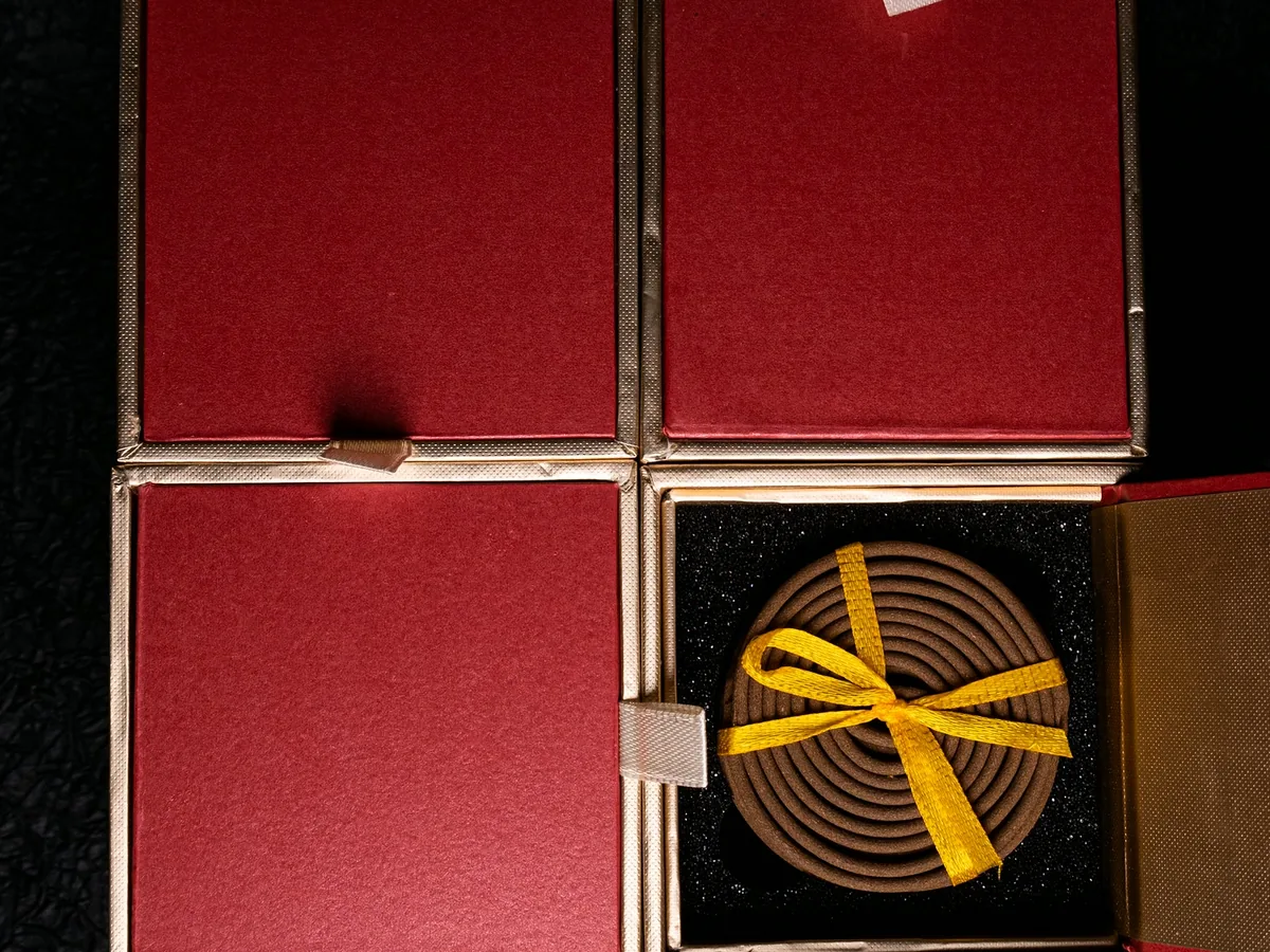 Four rigid gift boxes laid out in a block on dark paper, one open to show the coil inside