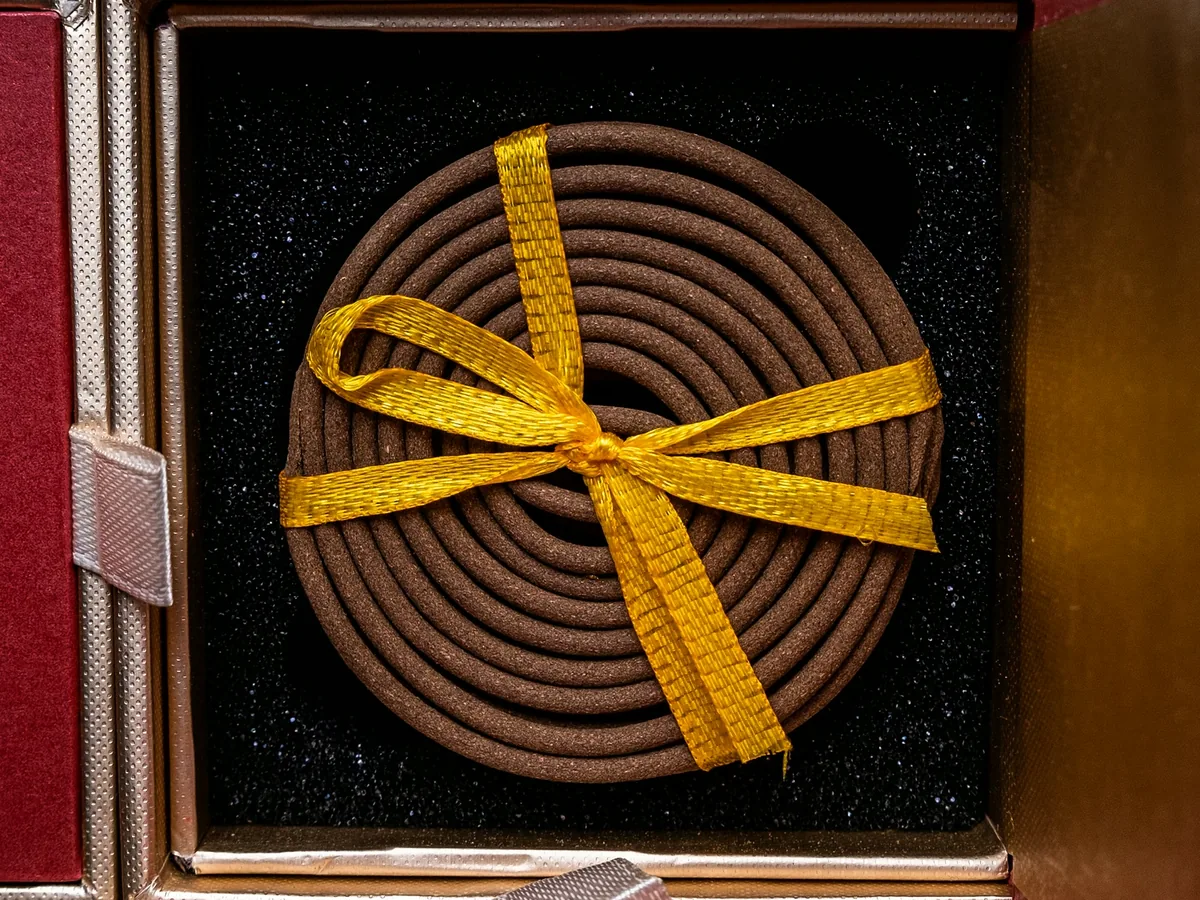 A rigid gift box open on black foam, one agarwood coil tied with a yellow ribbon seated in the well