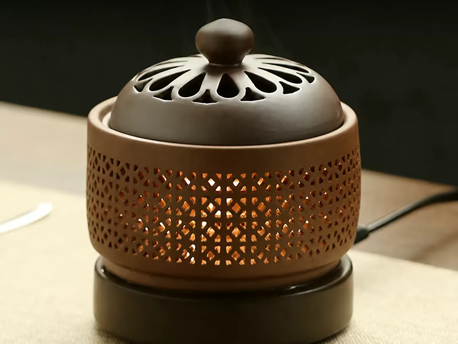 Ceramic temperature-controlled incense burner with a pierced lid, powered on, cable visible