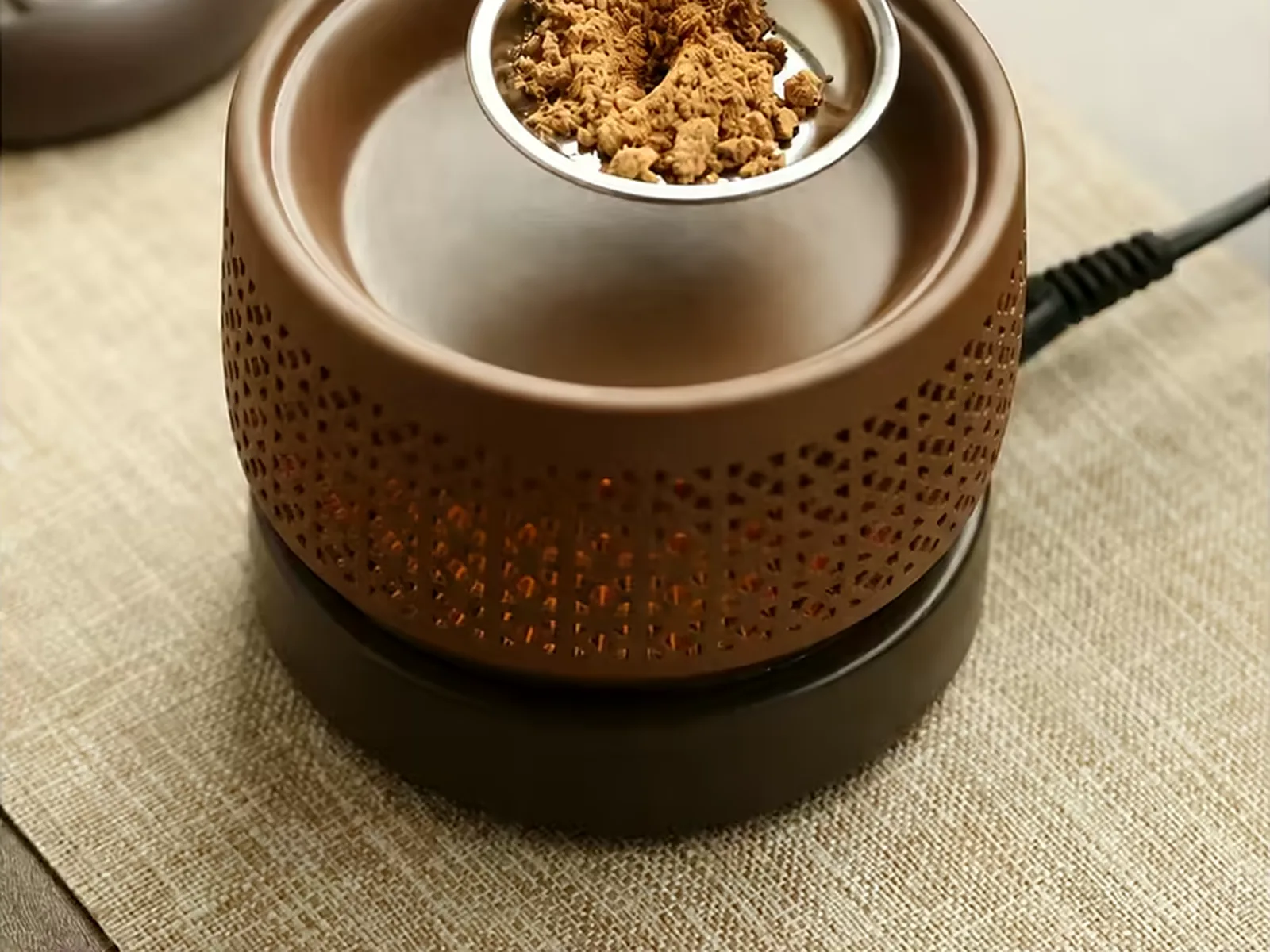 Agarwood powder being spooned onto the plate of a temperature-controlled incense burner