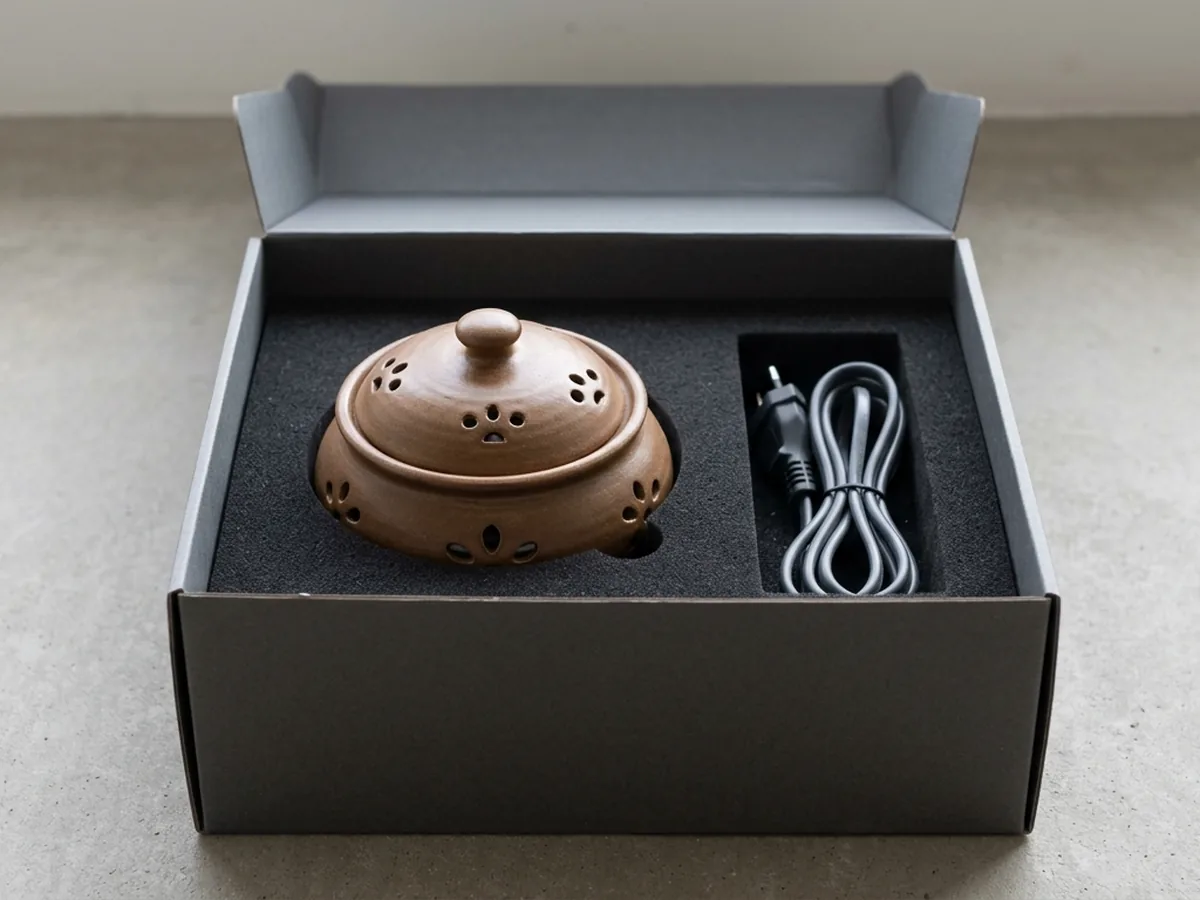 An open rigid box with a black moulded foam insert holding one ceramic electric incense burner and its coiled cable in a separate well