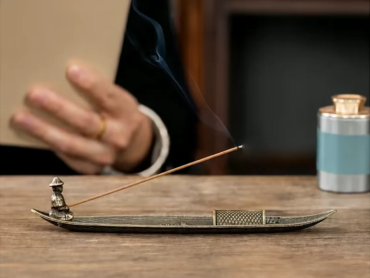 Hands working at a tablet on a desk with an incense stick burning on a boat holder alongside