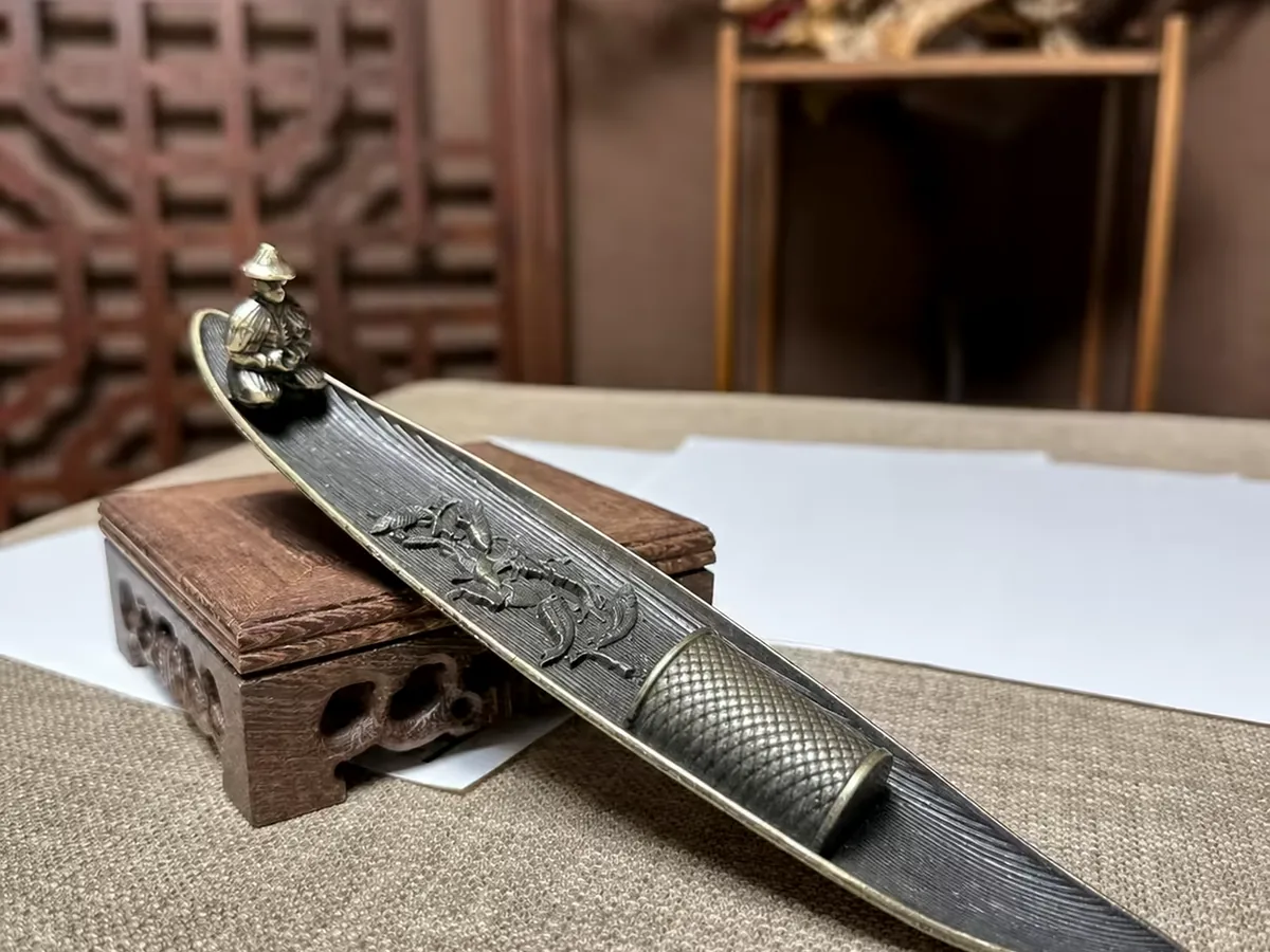 A boat-shaped incense holder on a linen desk mat with loose sheets of paper and a carved wooden box